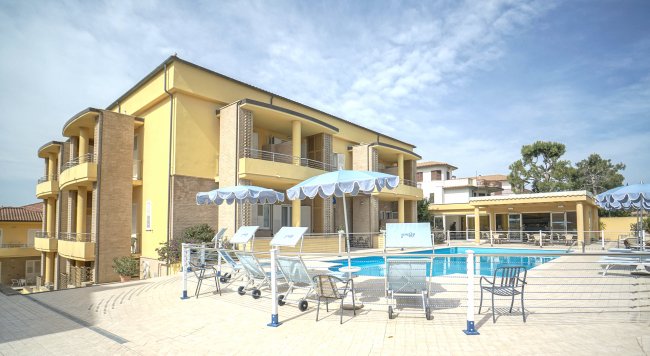 Edificio giallo a due piani con balconi, bordo piscina con ombrelloni blu.