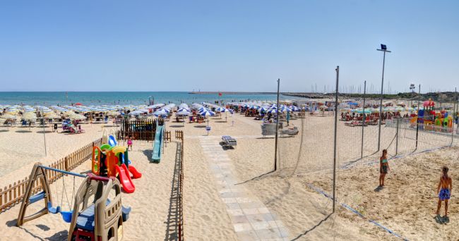 Una spiaggia con ombrelloni, giocattoli per bambini e persone che si rilassano al sole.