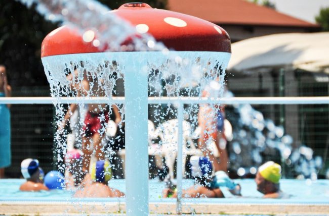 Una piscina con un fungo gigante da cui scorre acqua, persone nuotano intorno.
