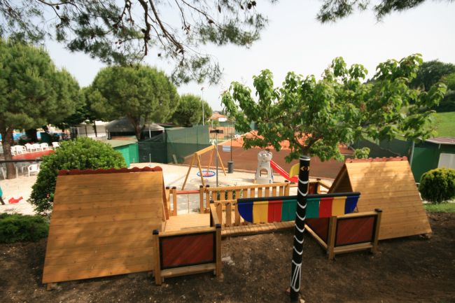 Parco giochi con strutture di legno e alberi verdi circostanti.