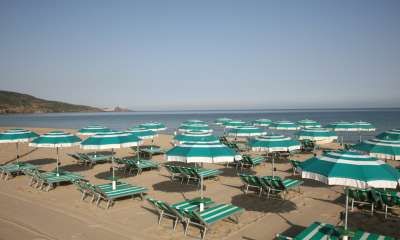Ombrelloni e sdraio verde acqua su una spiaggia sabbiosa con mare calmo.
