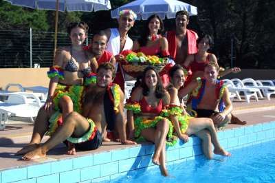 Un gruppo di persone in costumi colorati, seduti vicino a una piscina sotto ombrelloni.