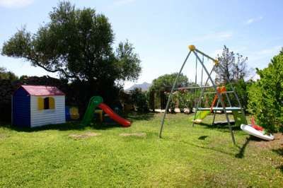 Un giardino con casetta da gioco, scivolo rosso e altalena.
