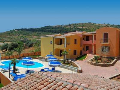 Complesso di edifici colorati con piscina e ombrelloni blu. Ambiente collinare.