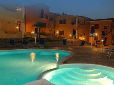 Piscina illuminata di notte con edifici colorati sullo sfondo.