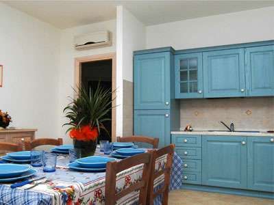 Cucina con mobili azzurri, tavolo apparecchiato e pianta al centro.