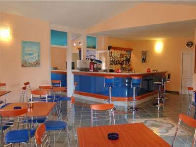 Un bar con tavoli e sedie colorati, un bancone blu e pareti arancioni.