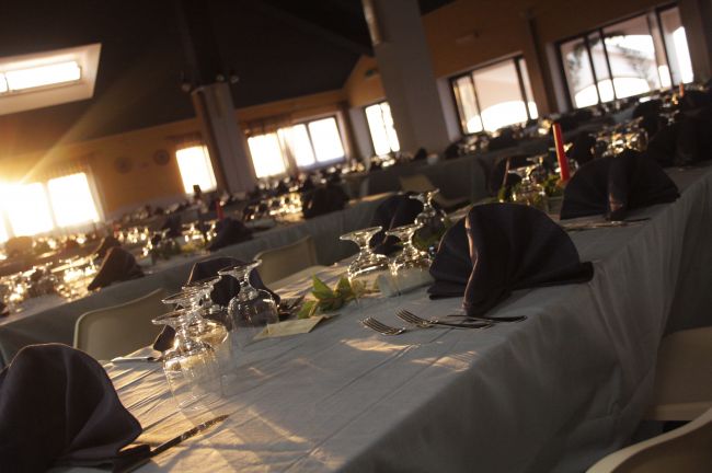 Tavoli apparecchiati per cena in una sala illuminata dalla luce del tramonto.