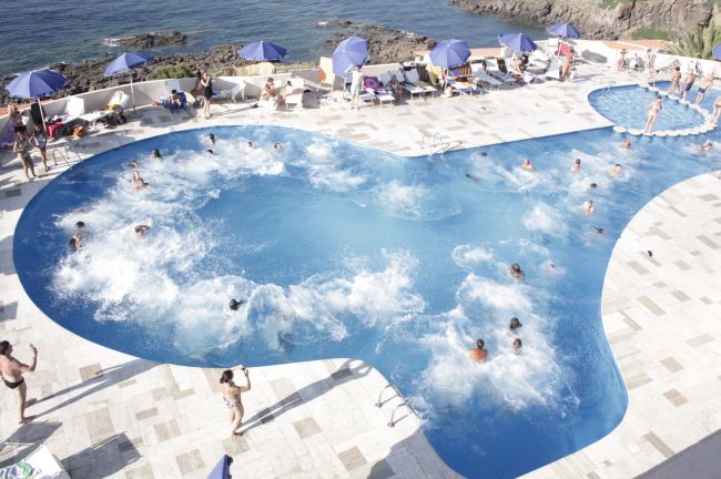 Una piscina affollata vicino al mare, con persone che si divertono in acqua.