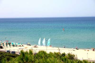 Spiaggia con ombrelloni verdi e vele bianche e azzurre viste dall'alto.