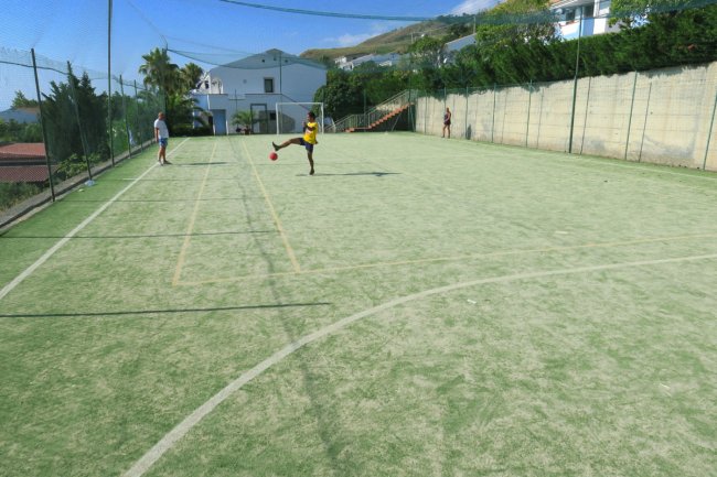 Un campo da calcetto all'aperto con rete di protezione, persona che calcia la palla.
