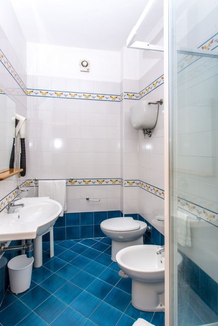 Bagno con pavimento blu, doccia, lavabo doppio e bidet. Piastrelle bianche decorate.