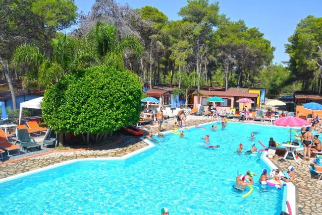 Piscina affollata con persone che nuotano e prendono il sole.