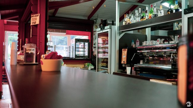 Bancone di un bar con macchina da caffè e bottiglie sugli scaffali.