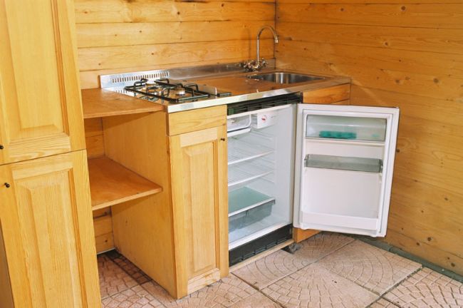 Mini cucina in legno con frigorifero aperto, lavello e fornelli.