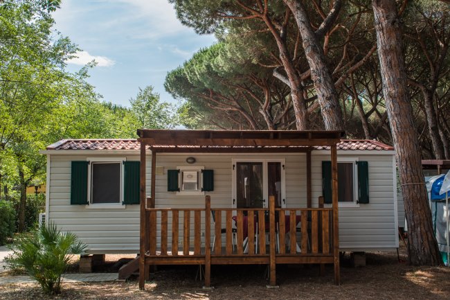 Una casa mobile con terrazza in legno, circondata da alberi alti.