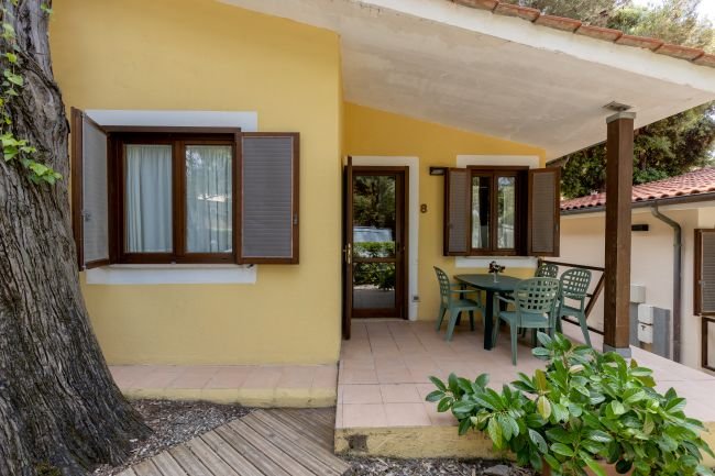 Casetta gialla con porta e finestre aperte su patio ombreggiato.