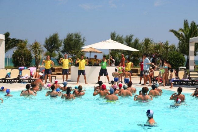 Piscina affollata con attività animate da istruttori in magliette gialle.