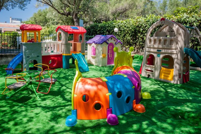 Area giochi all'aperto per bambini con strutture colorate su prato verde.