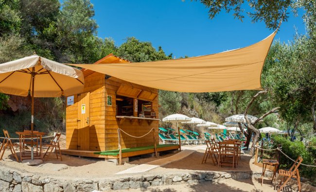 Chiosco in legno sulla spiaggia con tavoli e sedie, ombreggiato da teli.