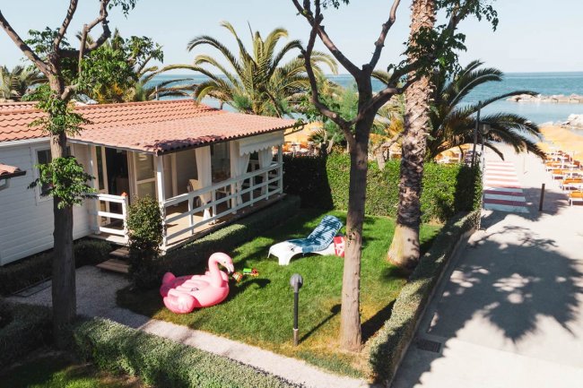Una casa al mare con giardino, palme, gonfiabile e sdraio. Vista del mare in lontananza.