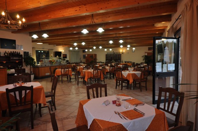 Interno di un ristorante con tavoli apparecchiati e soffitto in legno.