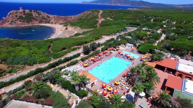 Vista aerea di un complesso con piscina, ombrelloni colorati, mare e vegetazione circostante.