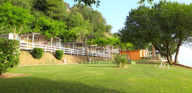 Complesso di bungalow su una collinetta verde, circondato da alberi e ampio prato.