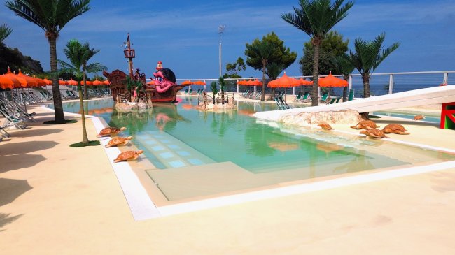 Piscina con scivolo, palme e decorazioni di tartarughe.
