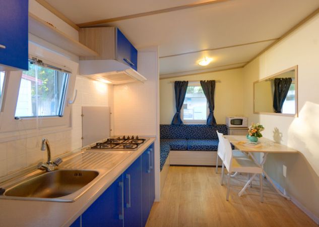 Interno cucina con mobili blu, tavolo da pranzo e divano vicino a finestre con tende.