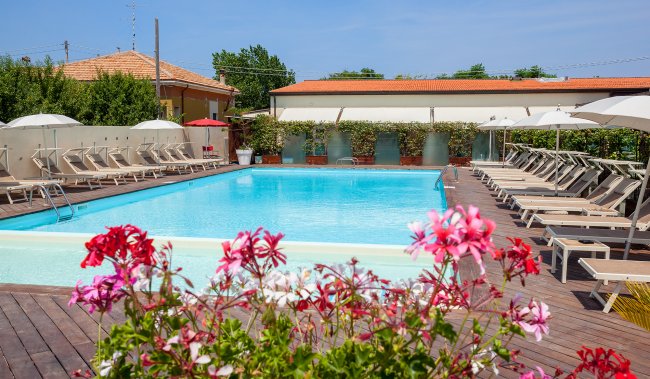 Piscina all'aperto con fiori sul bordo, circondata da lettini e ombrelloni.