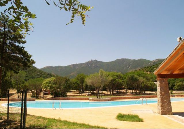 Piscina all'aperto circondata da alberi e colline sotto un cielo sereno.