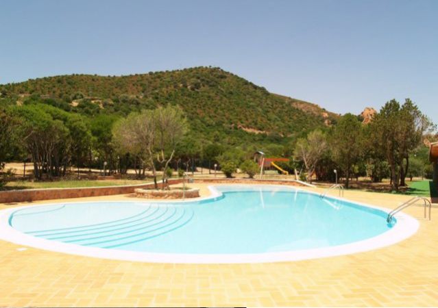 Piscina all'aperto con bordo di piastrelle, circondata da alberi e colline.