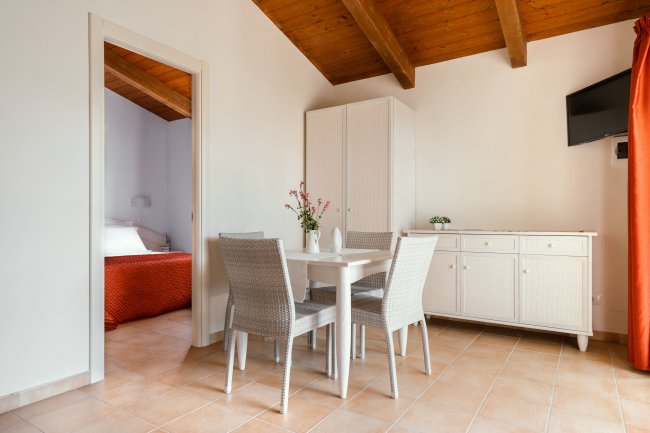 Sala da pranzo con tavolo e sedie di vimini, armadio bianco e vista su camera da letto.