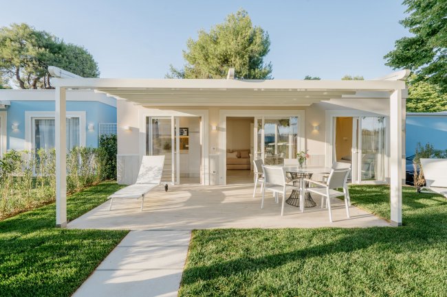 Bungalow moderno con patio, sedie e sdraio su prato verde.