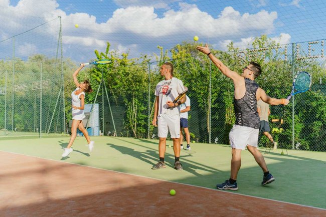 Persone che giocano a tennis su un campo all'aperto sotto un cielo nuvoloso.