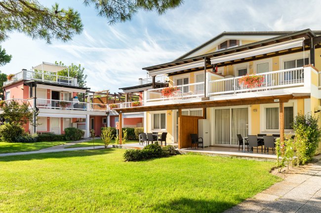 Complesso residenziale con appartamenti a due piani, balconi fioriti e giardino verde ben curato.
